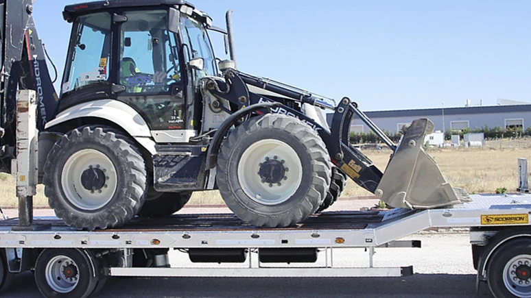 Scène extérieure sur chantier avec tractopelle chargé sur plateau de camion semi-remorque
