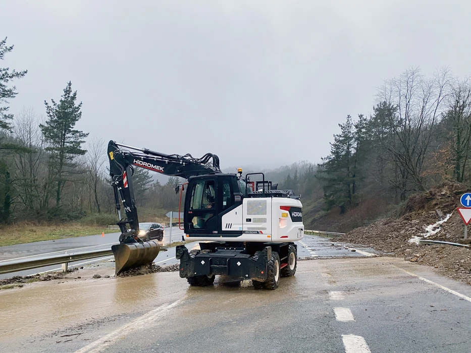 Chantier routier extérieur avec pelleteuse sur pneus Hidromek travaillant sur route mouillée