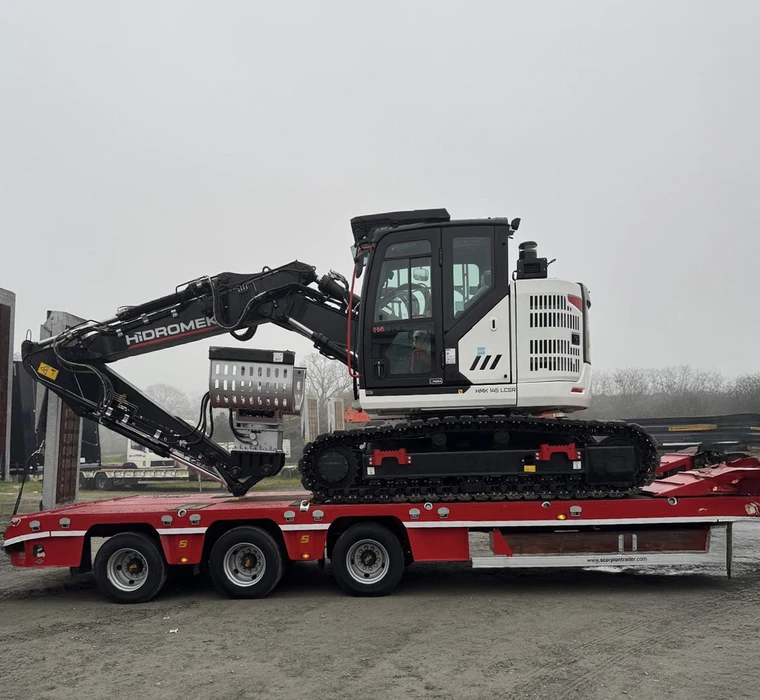 Scène extérieure avec pelleteuse sur chenilles Hidromek chargée sur semi-remorque rouge à trois essieux