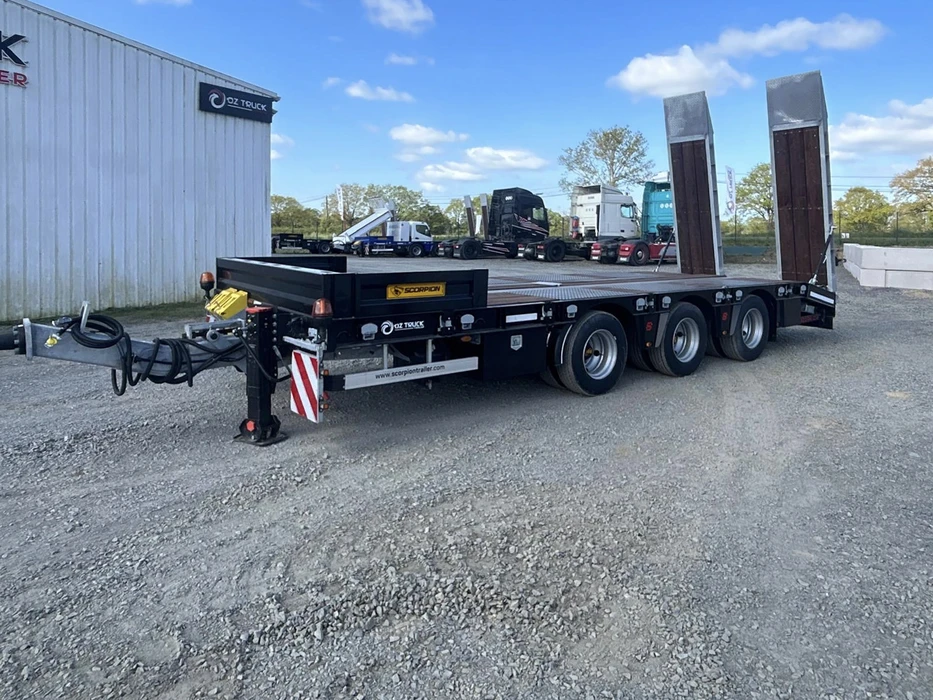 Scène extérieure d'un site industriel avec un camion semi-remorque transportant des grues mobiles sur plateau surbaissé