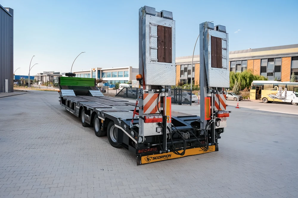 Scène extérieure d'un site de vente d'équipements de construction avec tracteur semi-remorque rouge et turquoise transportant une pelle sur roues