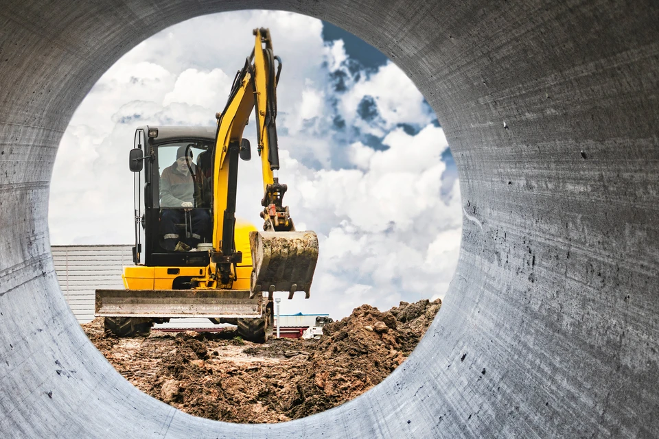 Chantier de construction en extérieur avec pelleteuse compacte orange et blanche équipée de chenilles caoutchouc, excavant le sol près d'une route goudronnée