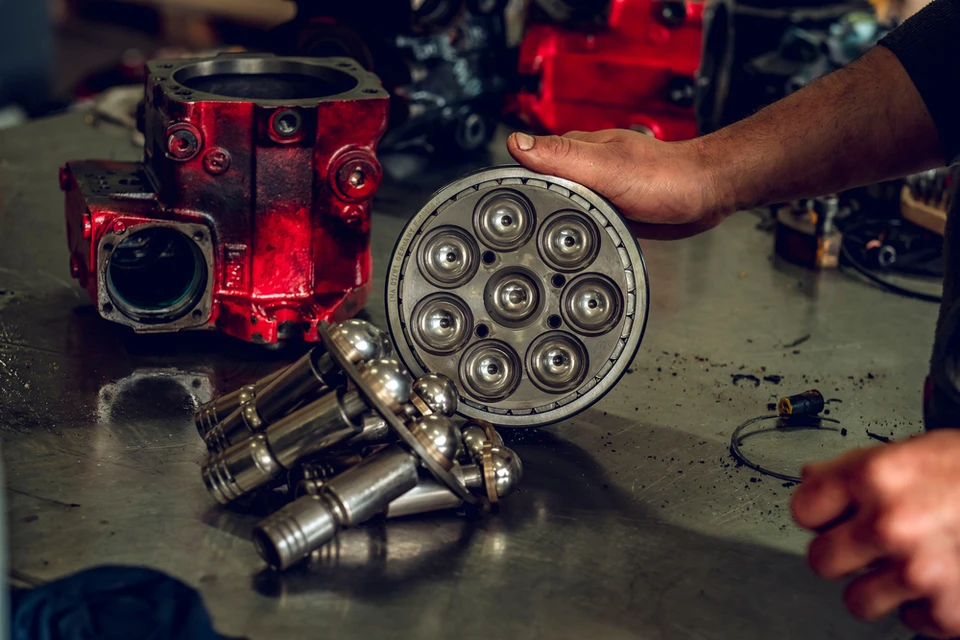 Atelier de réparation moto avec mécanicien en combinaison bleue accroupi, tenant une tablette numérique